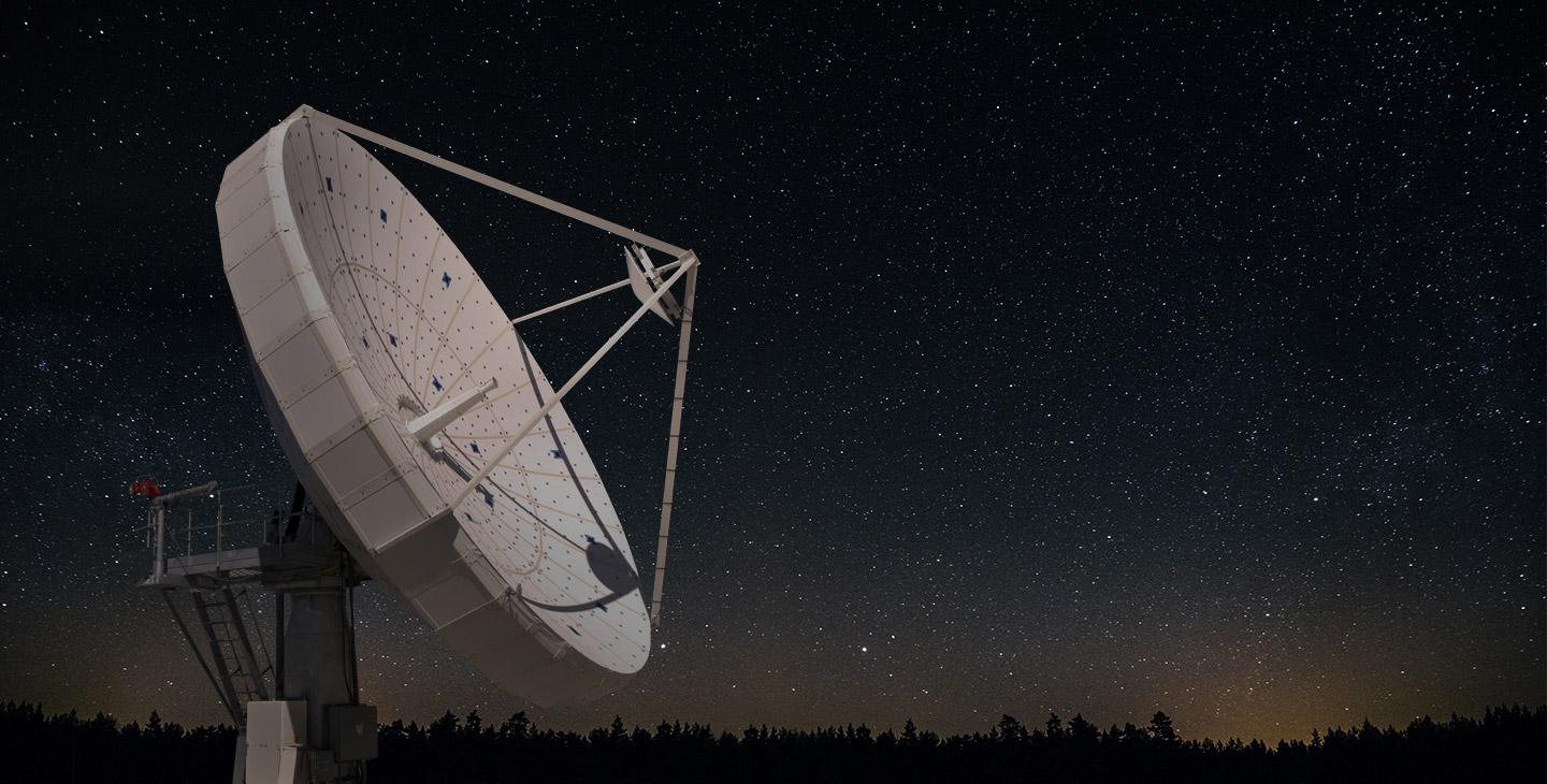 Large, white SATCOM antenna against a starry night sky